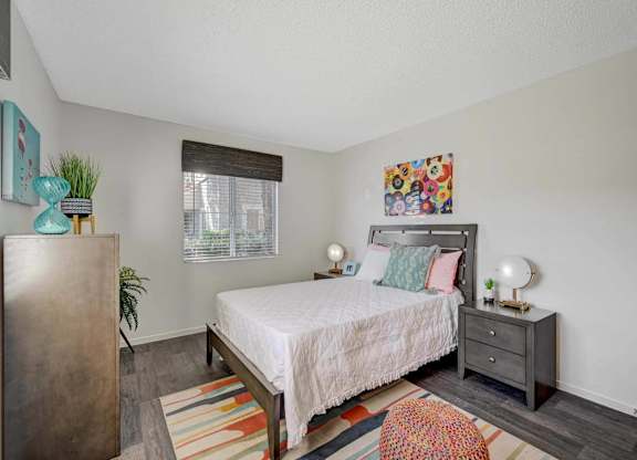 A bedroom with a bed, nightstand, and a plant.