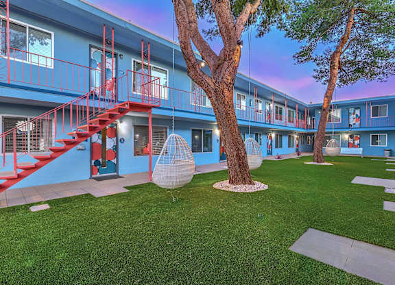 A tree in a courtyard with a red swing hanging from it.