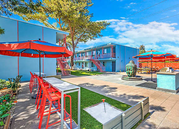 A patio with red chairs and tables is surrounded by a blue building.