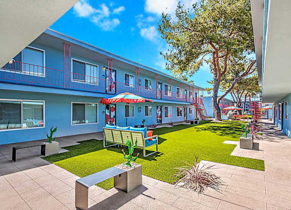 A sunny day at the courtyard of a blue building with a green lawn and a tree.