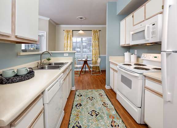 A kitchen with white appliances and a patterned rug on the floor.