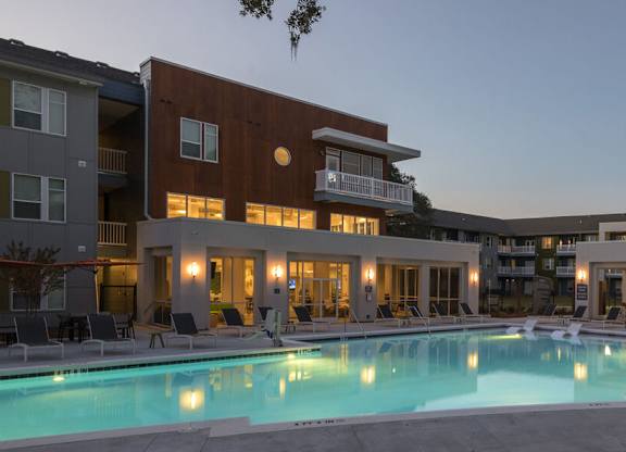A large swimming pool in front of a building with a lit up patio area.