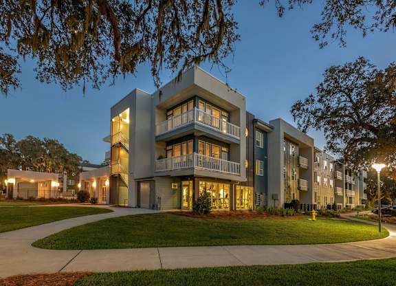 A modern apartment building with balconies and multiple stories is illuminated at dusk.