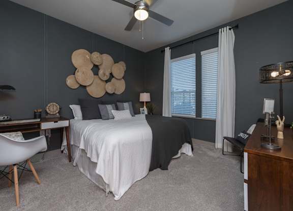 A bedroom with a bed, desk, chair, and a ceiling fan.