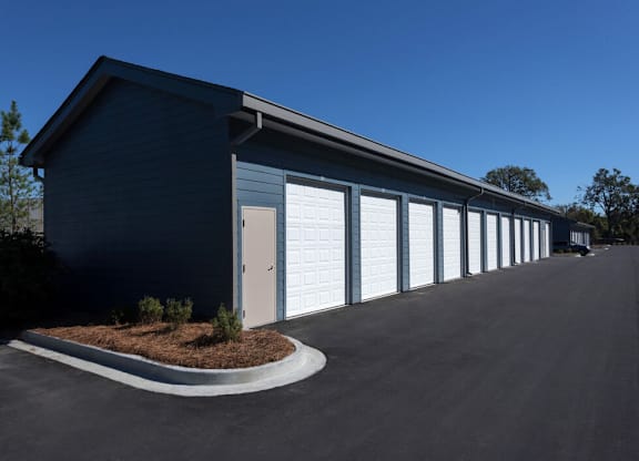 A blue building with white garage doors and a small garden in front.