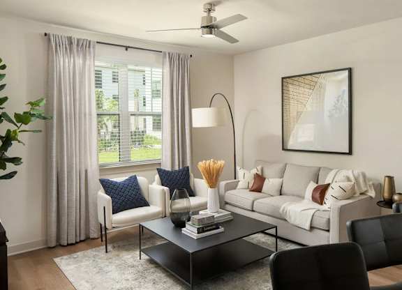 A living room with a grey couch, a black coffee table, and a large window with curtains.