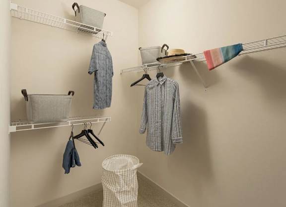 A white laundry room with clothes hanging on racks and a basket on the floor.