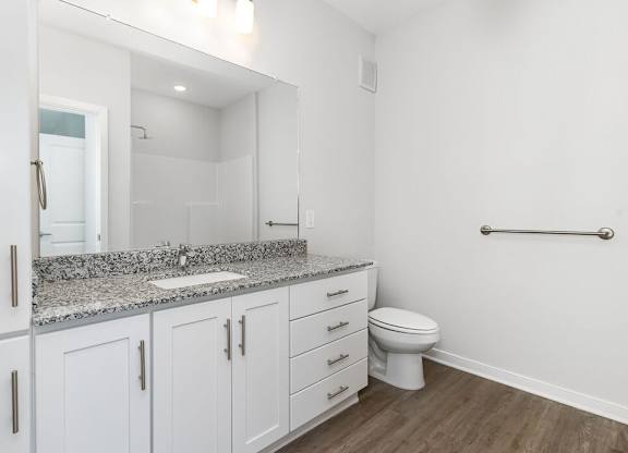 A white bathroom with a granite counter top and white cabinets.