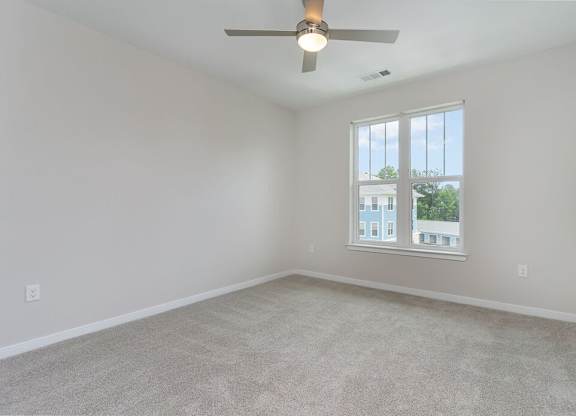 A room with a ceiling fan and a window overlooking a building.