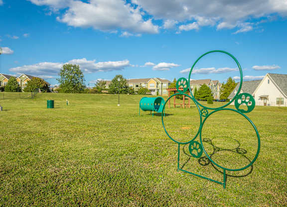 A green metal sculpture in a grassy field with houses in the background.