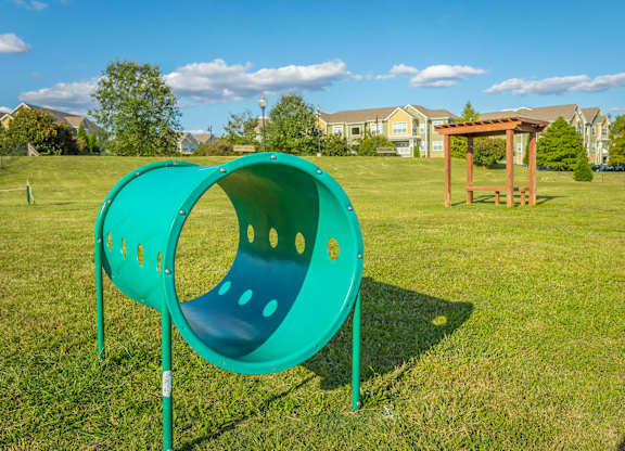 A green playground slide in a grassy area with a wooden structure in the background.