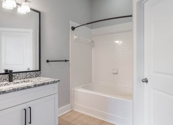 A white bathroom with a marble countertop and a white bathtub.