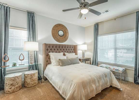 A bedroom with a large bed, a ceiling fan, and a window with curtains.