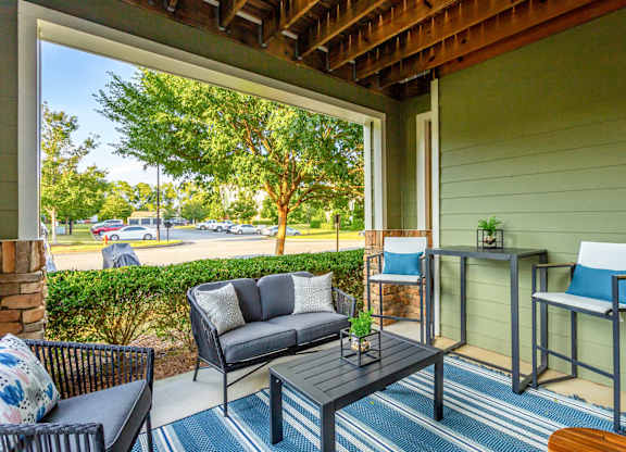 A patio with a black sofa, a black chair, and a small table with a plant on it.
