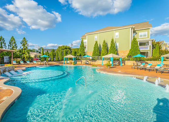 A large swimming pool with a fountain in the middle surrounded by a wooden deck and lounge chairs.