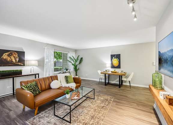 A living room with a brown couch, a glass coffee table, and a painting on the wall.