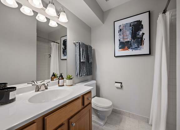 A bathroom with a white sink, toilet, and a painting on the wall.