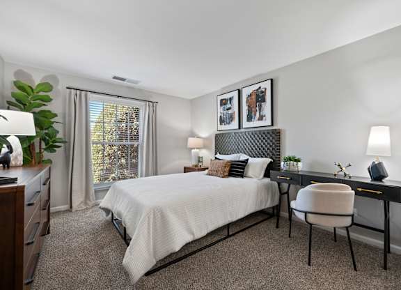 A bedroom with a bed, desk, chair, and window.
