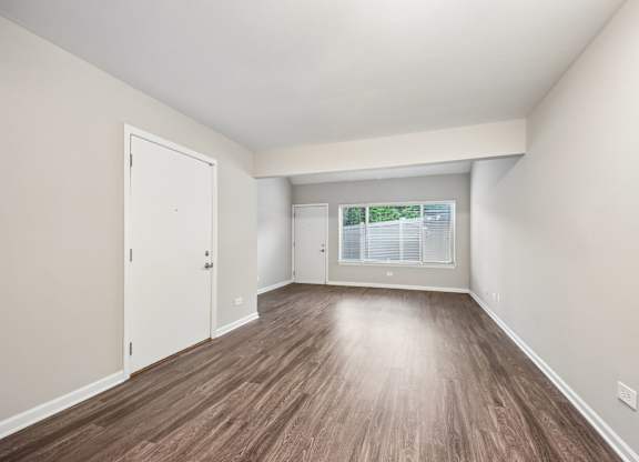 A room with wooden flooring and a window showing greenery outside.