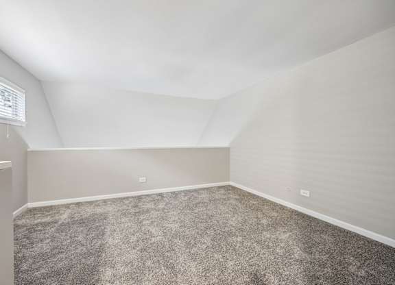 A room with a carpeted floor and a window with blinds.