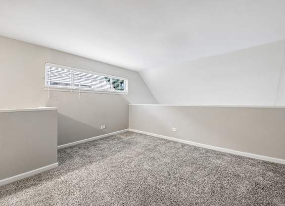 A room with a carpeted floor and a window with blinds.