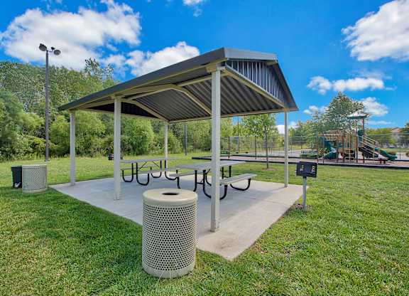 a picnic shelter with a table and benches in a park with a playground in the background at Evergreen Luxury Apartments, Indiana, 46410