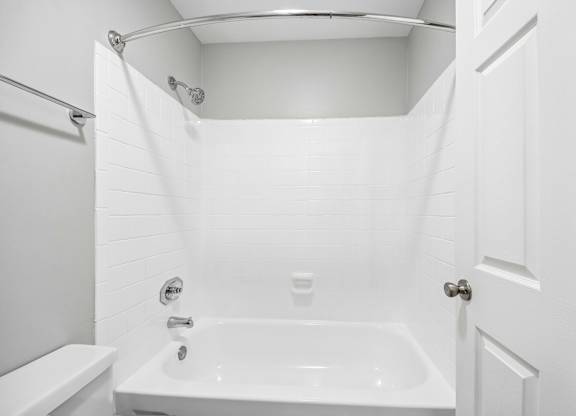 A white bathroom with a tub, toilet, and shower.