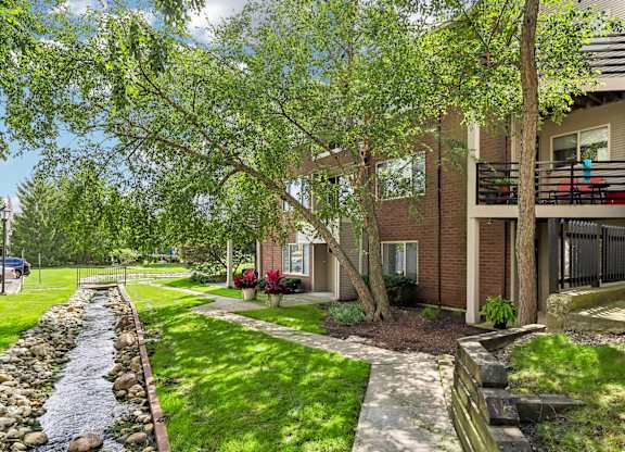 A stream of water runs through a grassy area in front of a row of houses.