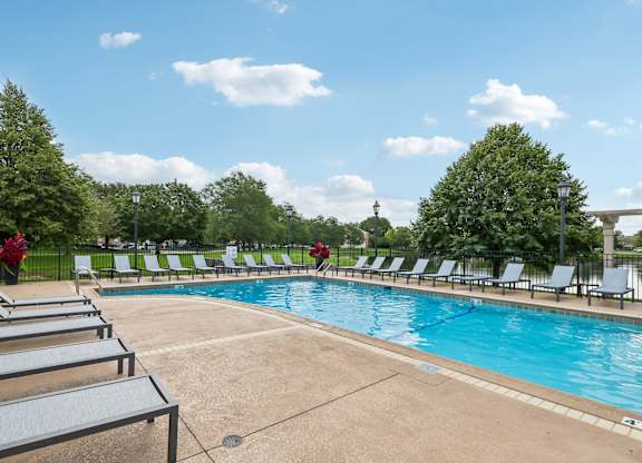 A pool surrounded by lounge chairs and trees.