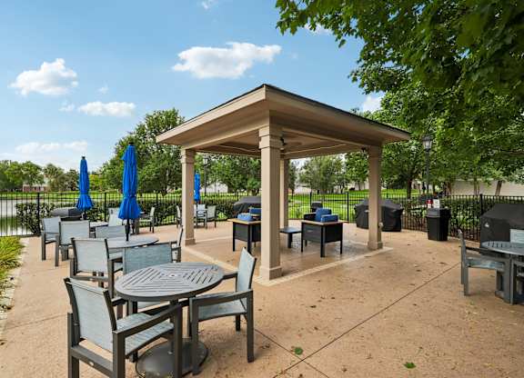 A gazebo with a table and chairs is surrounded by trees.