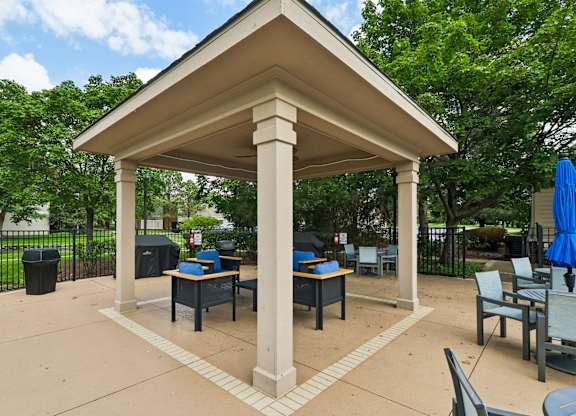 A gazebo with a table and chairs is surrounded by trees.