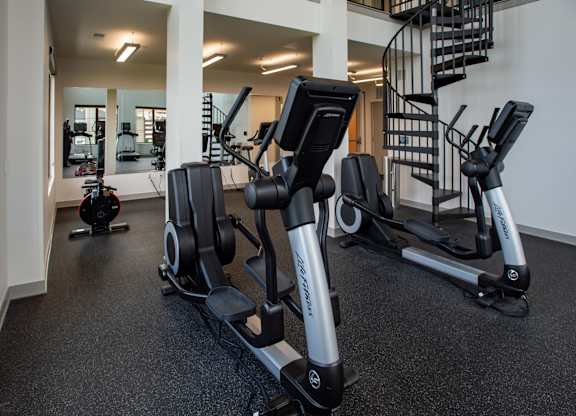 a row of exercise bikes in a gym with a spiral staircase at 42 Hundred On The Lake, St Francis, WI, 53235