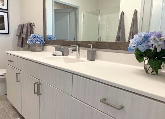 A bathroom with a white countertop and a large mirror. at Elevate Apartments, Madison, WI