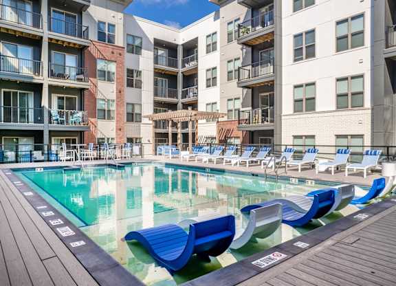 A pool with blue lounge chairs and a wooden deck in front of apartment buildings. at Elevate Apartments, Wisconsin, 53718