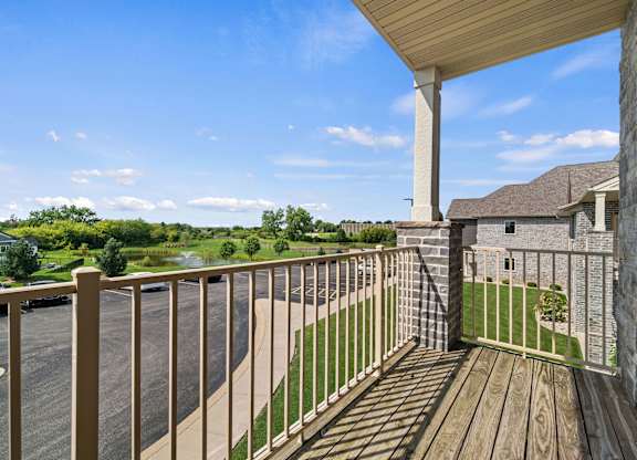 A wooden deck with a white railing overlooks a parking lot and a house.