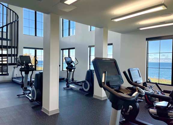a gym with cardio equipment and windows overlooking the lake at 42 Hundred On The Lake, St Francis, WI, 53235
