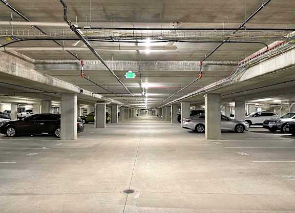 a parking garage with cars and a green exit sign at 42 Hundred On The Lake, St Francis, WI, 53235