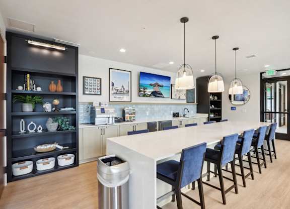 A modern kitchen with a long white island and blue chairs.