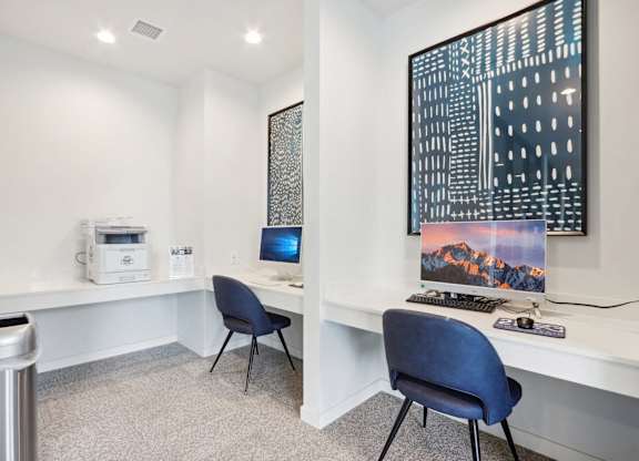 A room with a desk, chairs, and a large picture on the wall.