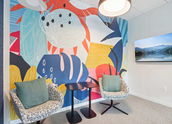 A room with a colorful mural and two chairs with green pillows.