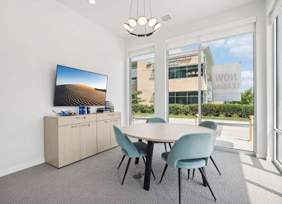 A conference room with a large screen on the cabinet and a table with four chairs.