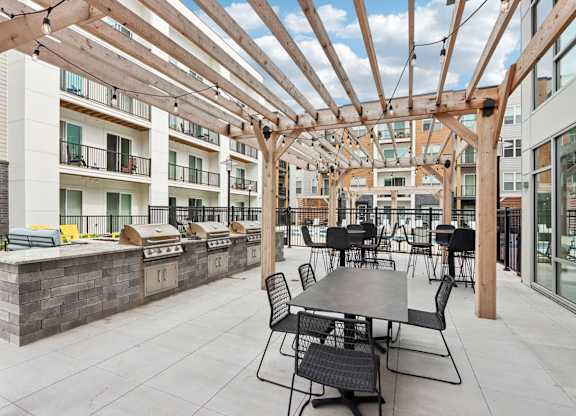 A patio with tables and chairs is covered by a wooden roof.