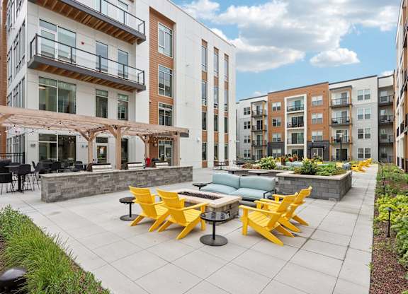A patio with yellow chairs and tables is surrounded by apartment buildings.