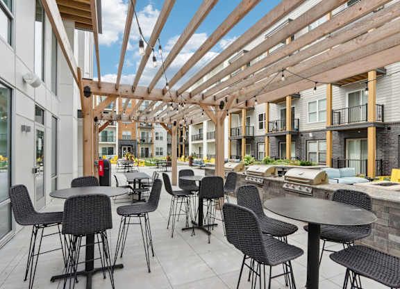 A patio with tables and chairs is covered by a wooden roof.