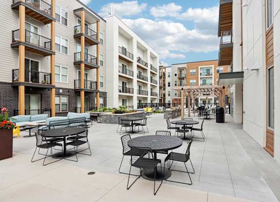 A patio area with tables and chairs is surrounded by apartment buildings.