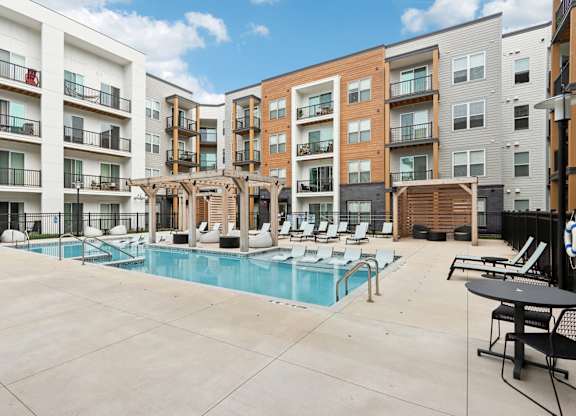 A large outdoor pool area with lounge chairs and a wooden pergola.