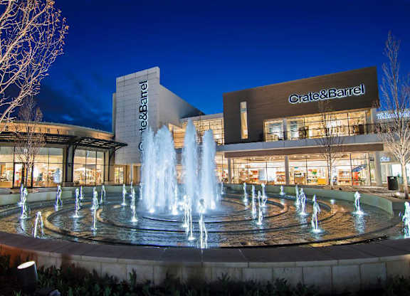 A Crate & Barrel store is lit up at night with a fountain in front.