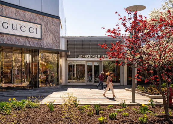 A woman walks past a Gucci store and a Johnston & Murphy store.