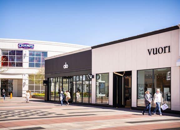 A street view of a Champs and a Vuori store with people walking by.