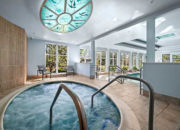 A round glass window with a fish design is above a hot tub.